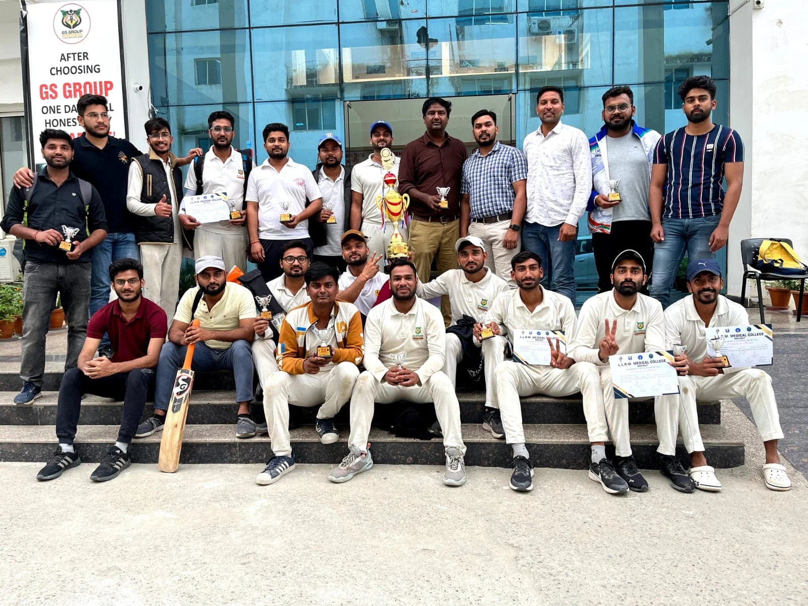 21 people standing with one cricket bat and one trophy